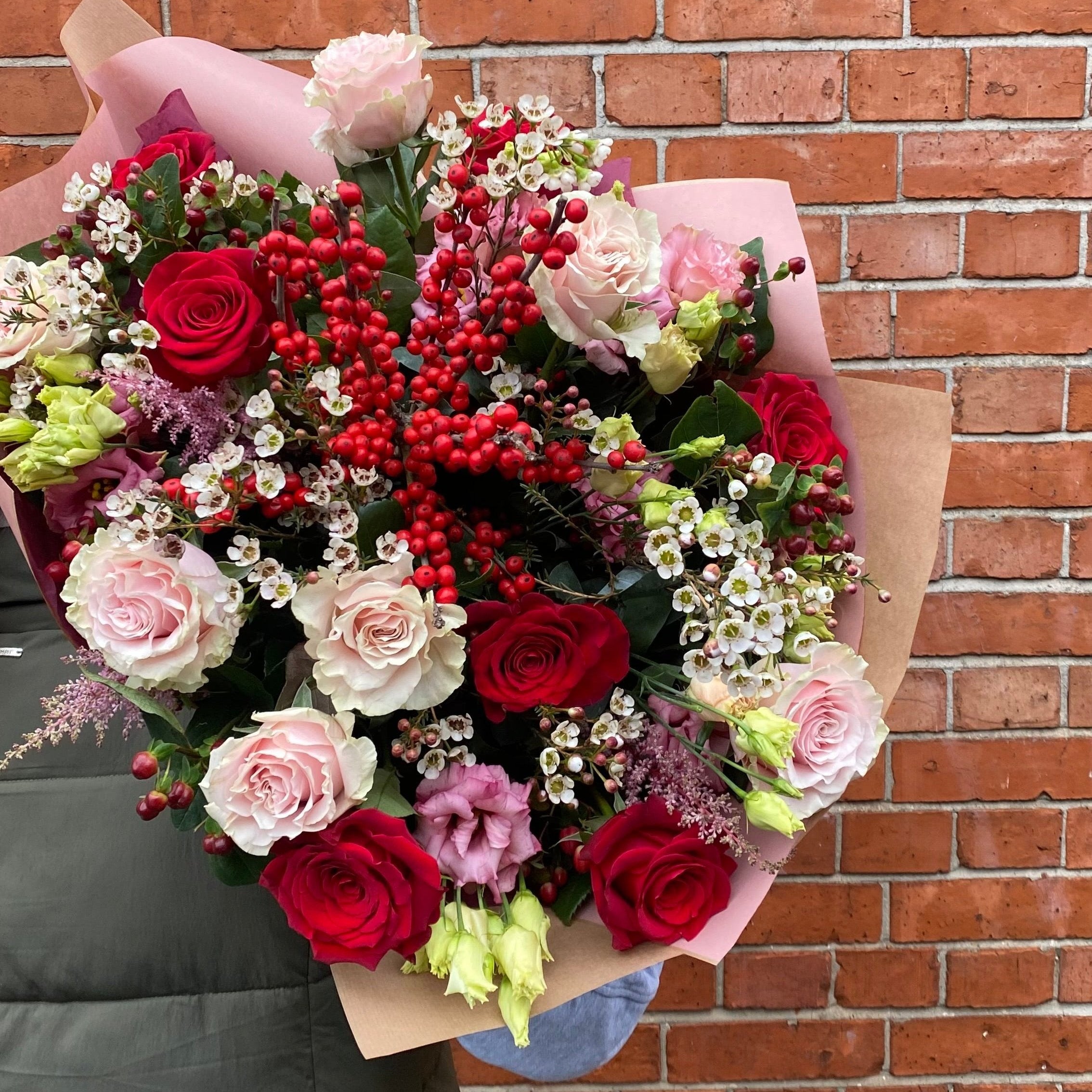 A bouquet of assorted flowers including red and white roses, greenery, and other seasonal flowers, wrapped in brown paper with a card.